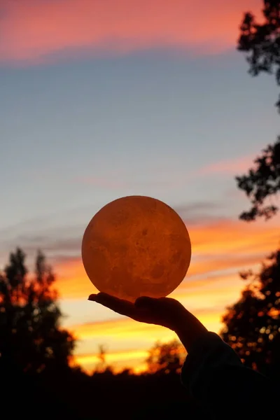 Moon in the hand on red sunrise background. Moon bedside lamp on the sky