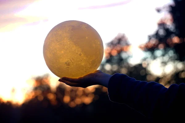 Moon in the hand on red sunrise background. Moon bedside lamp on the sky