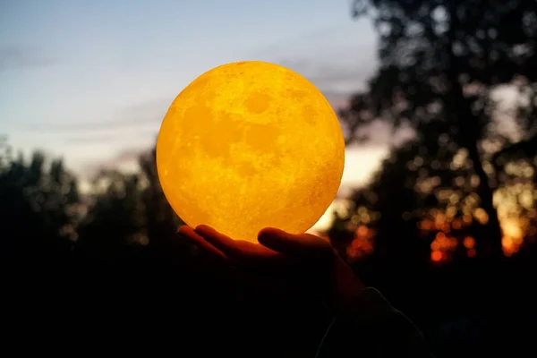 Moon in the hand on red sunrise background. Moon bedside lamp on the sky