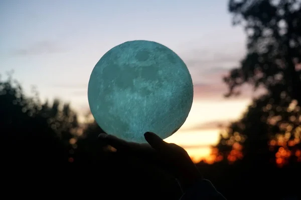 Moon in the hand on red sunrise background. Moon bedside lamp on the sky