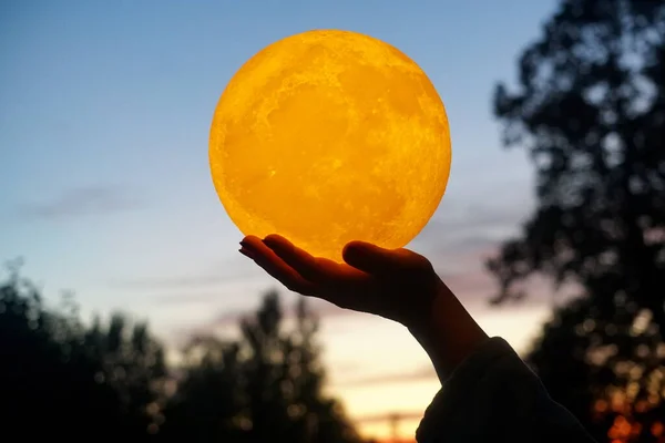 Moon in the hand on red sunrise background. Moon bedside lamp on the sky