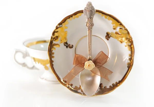 Silver teaspoon with a bow on golden background cup saucer. — Stock Photo, Image