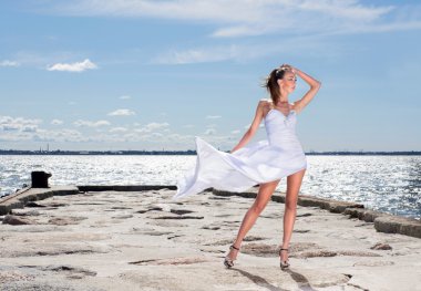 Young sexy girl in a white dress standing on a pier