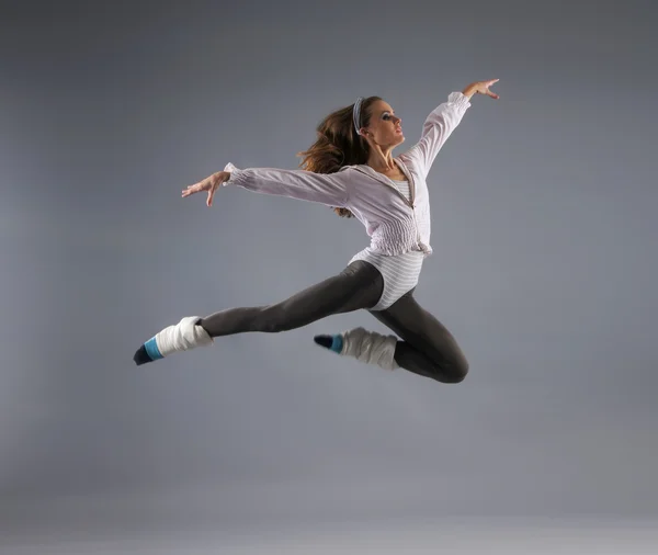 Young, attractive, sporty and sexy modern dancer jumping over grey background — Stock Photo, Image
