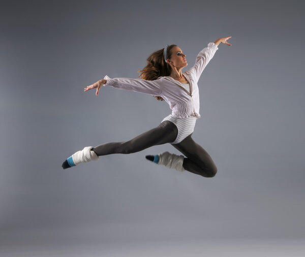 Young, attractive, sporty and sexy modern dancer jumping over grey background