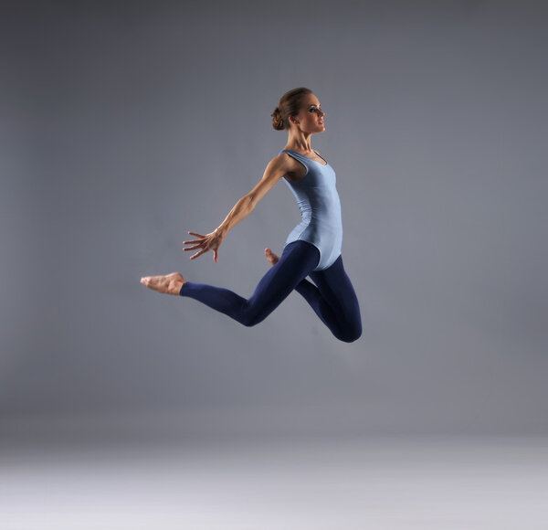 Young, attractive, sporty and sexy modern dancer jumping over grey background