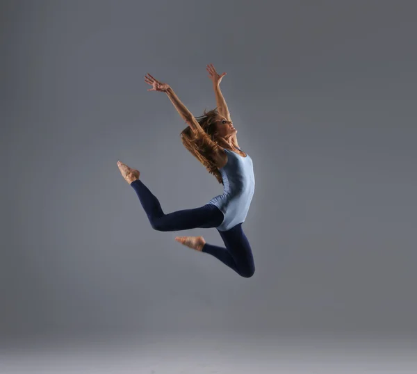 Bailarina moderna joven, atractiva, deportiva y sexy saltando sobre fondo gris — Foto de Stock