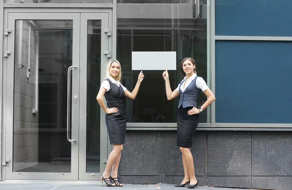 Two young attractive business women are showing the blank banner — Stock Photo, Image