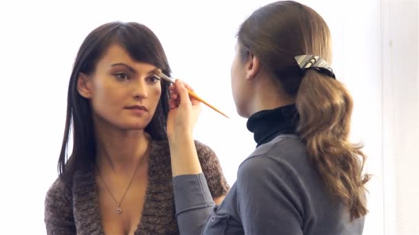 Макияж художник наносит косметику на лицо красивой модели — стоковое видео
