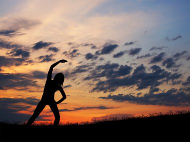 gün batımı ba üzerinde yoga egzersiz yaparak genç bir kadın silueti