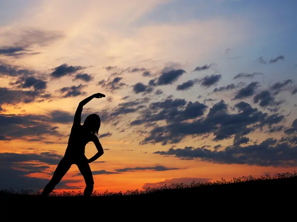 Gün batımı ba üzerinde yoga egzersiz yaparak genç bir kadın silueti — Stok fotoğraf