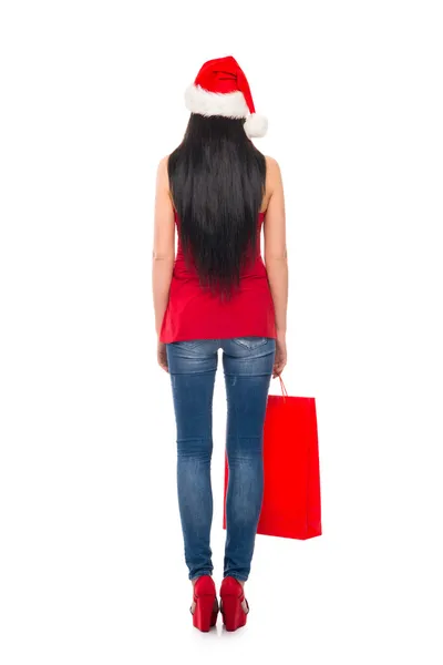 Una mujer feliz en un sombrero de Navidad sosteniendo una bolsa de compras roja —  Fotos de Stock