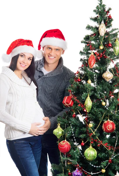 Una mujer embarazada y un hombre feliz posando cerca del árbol de Navidad — Foto de Stock