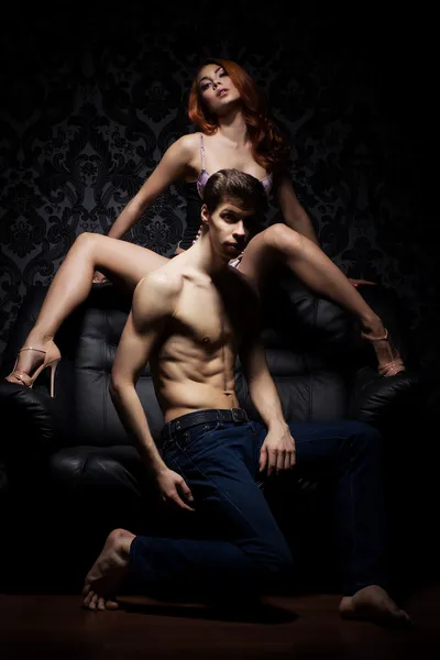 Um casal jovem e sexy em lingerie em um sofá preto — Fotografia de Stock