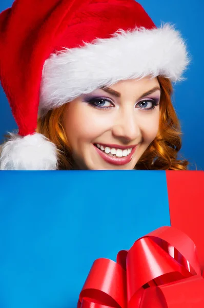 Uma mulher feliz em um chapéu de Natal vermelho em um fundo azul — Fotografia de Stock