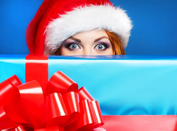 Uma mulher feliz em um chapéu de Natal vermelho em um fundo azul — Fotografia de Stock