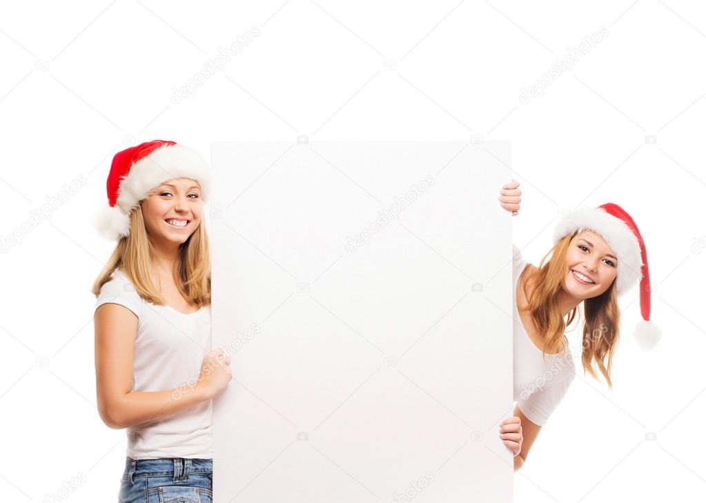 Three happy teenagers in Christmas hats pointing on a large blan