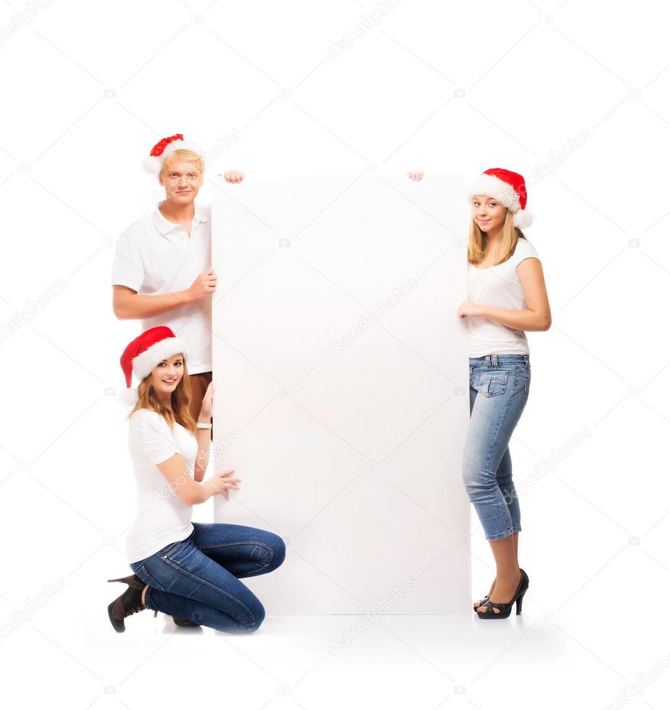 Three happy teenagers in red Christmas hats posing next to a white banner