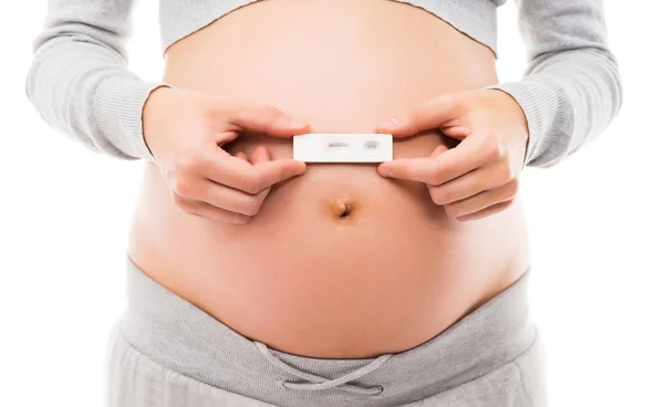 一个怀孕的女人，牵着一个怀孕测试的肚子 — 图库照片
