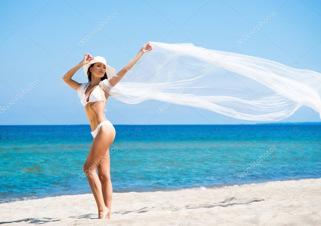 A young brunette woman in a white swimsuit relaxing on the beach