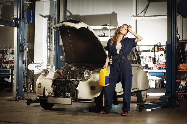 Mujer joven y sexy reparando un coche retro en un garaje — Foto de Stock