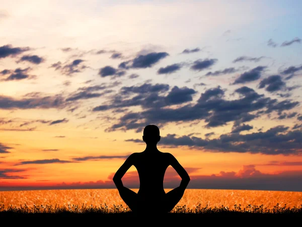 Silueta mladé ženy meditaci na západ slunce — Stock fotografie