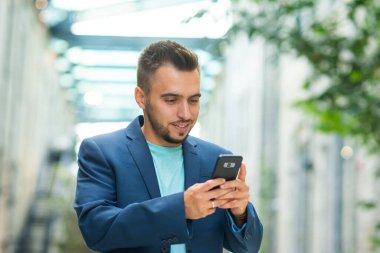 Genç ve başarılı bir iş adamı akıllı telefon kullanarak dışarıda çalışıyor. Sıradan giysili bir adam. İş, serbest meslek ve uzak çalışma.