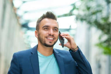 Genç ve başarılı bir iş adamı akıllı telefon kullanarak dışarıda çalışıyor. Sıradan giysili bir adam. İş, serbest meslek ve uzak çalışma.
