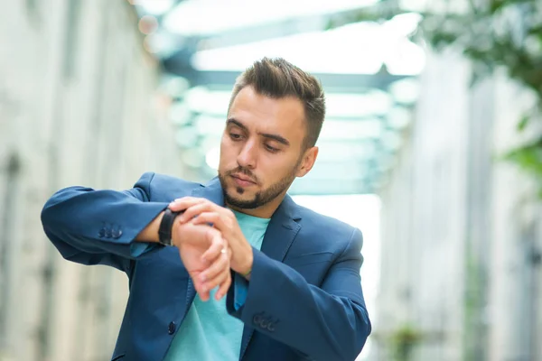 Um jovem empresário de sucesso está trabalhando ao ar livre usando smartwatch. Um homem de fato casual. Trabalho de negócios, freelance e remoto. — Fotografia de Stock