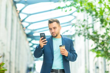 Genç ve başarılı bir iş adamı akıllı telefon kullanarak dışarıda çalışıyor. Sıradan giysili bir adam. İş, serbest meslek ve uzak çalışma.