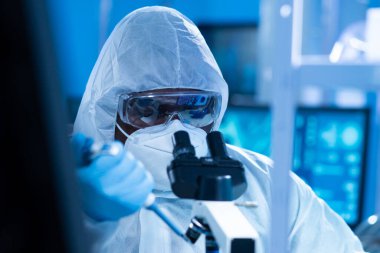 Koruyucu kıyafetli Afrikalı-Amerikalı doktor modern bir laboratuvarda bilimsel deneyler yapıyor ve aşı geliştiriyor. Laboratuvar asistanı iş yerinde. Bilim ve tıp kavramı.