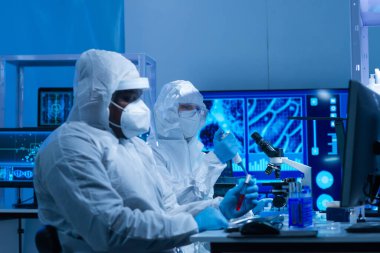 Koruyucu kıyafetli Afrikalı-Amerikalı doktor modern bir laboratuvarda bilimsel deneyler yapıyor ve aşı geliştiriyor. Laboratuvar asistanı iş yerinde. Bilim ve tıp kavramı.