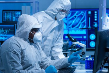 Koruyucu kıyafetli Afrikalı-Amerikalı doktor modern bir laboratuvarda bilimsel deneyler yapıyor ve aşı geliştiriyor. Laboratuvar asistanı iş yerinde. Bilim ve tıp kavramı.