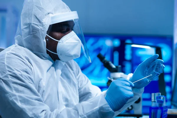 Koruyucu kıyafetli Afrikalı-Amerikalı doktor modern bir laboratuvarda bilimsel deneyler yapıyor ve aşı geliştiriyor. Laboratuvar asistanı iş yerinde. Bilim ve tıp kavramı.