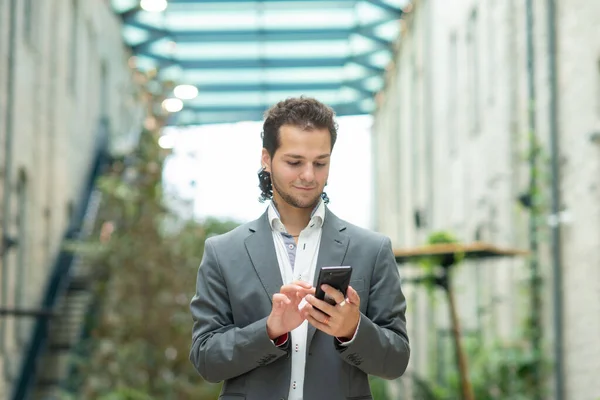 Ένας νεαρός επιτυχημένος επιχειρηματίας εργάζεται σε εξωτερικούς χώρους χρησιμοποιώντας smartphone. Ένας άντρας με ένα απλό ντύσιμο. Επαγγελματική, ανεξάρτητη και εξ αποστάσεως εργασία. — Φωτογραφία Αρχείου