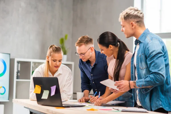 El equipo de jóvenes y confiados startupers está trabajando en la mesa de la oficina, discutiendo la estrategia y el plan de desarrollo de la empresa. Negocios, innovación, lluvia de ideas y trabajo en equipo. —  Fotos de Stock