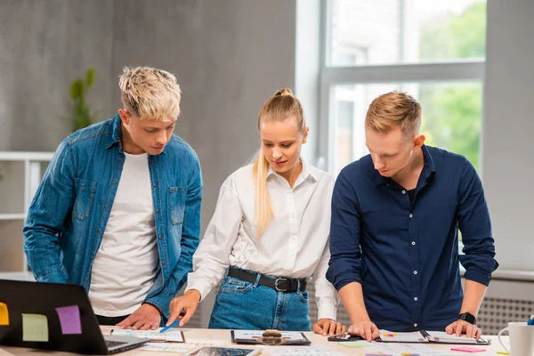 Team of young and confident startupers is working at the table in the office, discussing the strategy and development plan of the company. Business, innovation, brainstorming and teamwork. — Stock Photo, Image