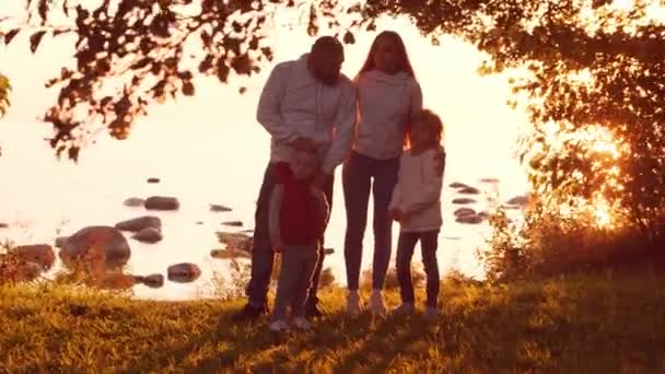 Milující rodinné procházky po venkově během západu slunce. Máma s tátou se objímají a hrají si se synem a dcerou. Koncept lásky, rodičovské péče a dětí. — Stock video