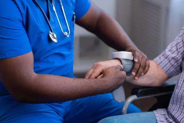 Afro-Amerikalı bakıcı engelli yaşlı adamın kan basıncını ölçüyor. Bakımevindeki profesyonel hemşire ve özürlü hasta. Yardım, rehabilitasyon ve sağlık. — Stok fotoğraf