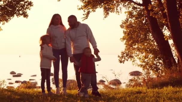 Amar los paseos familiares en el campo durante el atardecer. Mamá y papá abrazan y juegan con su hijo y su hija. El concepto de amor, cuidado parental e hijos. — Vídeos de Stock