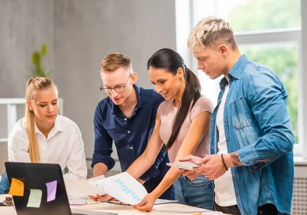 El equipo de jóvenes y confiados startupers está trabajando en la mesa de la oficina, discutiendo la estrategia y el plan de desarrollo de la empresa. Negocios, innovación, lluvia de ideas y trabajo en equipo. — Foto de Stock