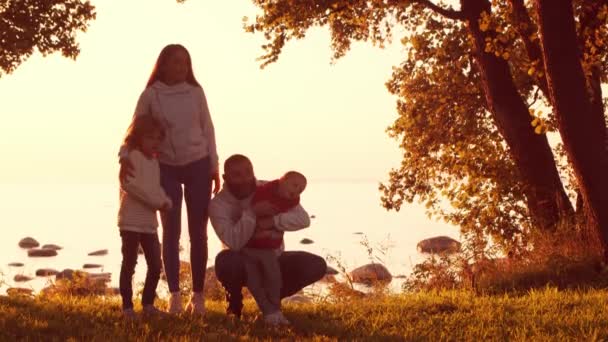 Sevgi dolu aile gün batımında kırsalda dolaşır. Anne ve baba, oğulları ve kızlarıyla sarılıp oynuyorlar. Aşk kavramı, aile bakımı ve çocuklar.. — Stok video