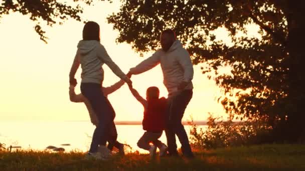 Amar los paseos familiares en el campo durante el atardecer. Mamá y papá abrazan y juegan con su hijo y su hija. El concepto de amor, cuidado parental e hijos. — Vídeos de Stock