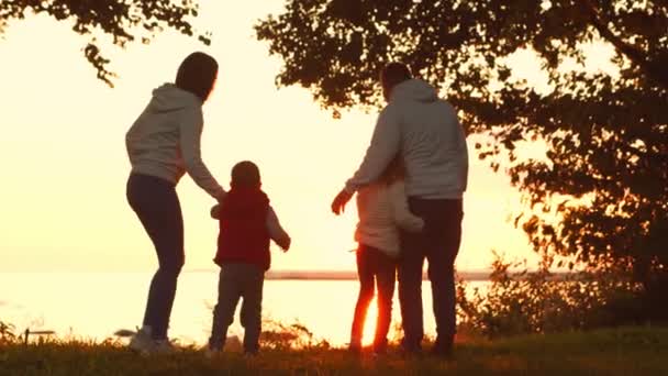 Liebevolle Familienspaziergänge in der Natur während des Sonnenuntergangs. Mama und Papa umarmen und spielen mit ihrem Sohn und ihrer Tochter. Das Konzept der Liebe, der elterlichen Sorge und der Kinder. — Stockvideo