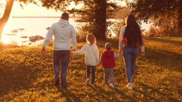 Amar los paseos familiares en el campo durante el atardecer. Mamá y papá abrazan y juegan con su hijo y su hija. El concepto de amor, cuidado parental e hijos. — Vídeos de Stock