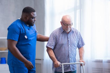 Bakıcı yaşlı adama Walker 'la yürümeyi öğretiyor. Bakımevindeki profesyonel hemşire ve hasta. Yardım, rehabilitasyon ve sağlık.