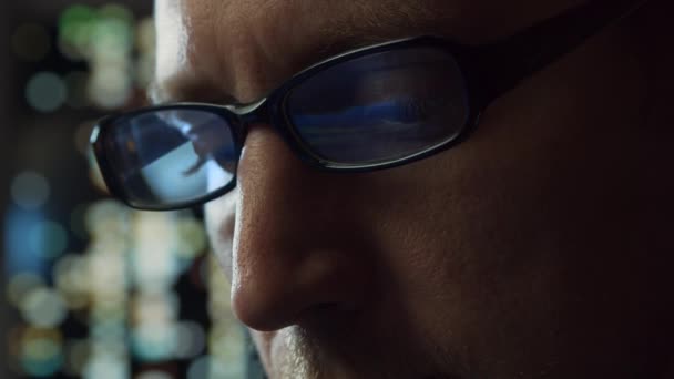 Retrato de cerca de un joven que trabaja en la computadora. La pantalla del ordenador portátil se refleja en las gafas. Luces nocturnas en el fondo. Concepto de negocio, codificación e intercambio. — Vídeo de stock