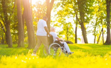 Bakıcı ve tekerlekli sandalyedeki yaşlı adam. Profesyonel hemşire ve hasta gün batımında parkta yürüyorlar. Yardım, rehabilitasyon ve sağlık hizmetleri.