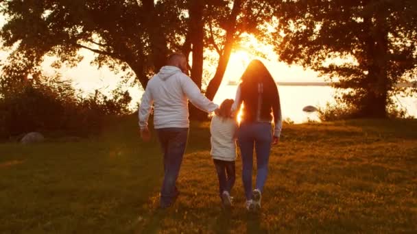 Amar los paseos familiares en el campo durante el atardecer. Mamá y papá abrazan y juegan con su hijo y su hija. El concepto de amor, cuidado parental e hijos. — Vídeos de Stock