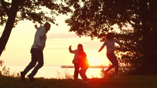 日落时，有爱心的家人在乡间散步。妈妈和爸爸抱着他们的儿子和女儿玩耍。爱情、父母照料和儿童的概念. — 图库视频影像